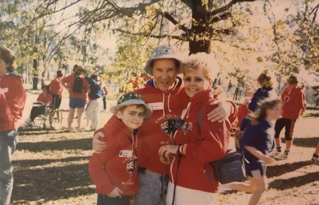 A child, a man, and Camp Quality founder, Vera Entwistle, pose for a photograph at the first Camp Quality Family Camp in 1988