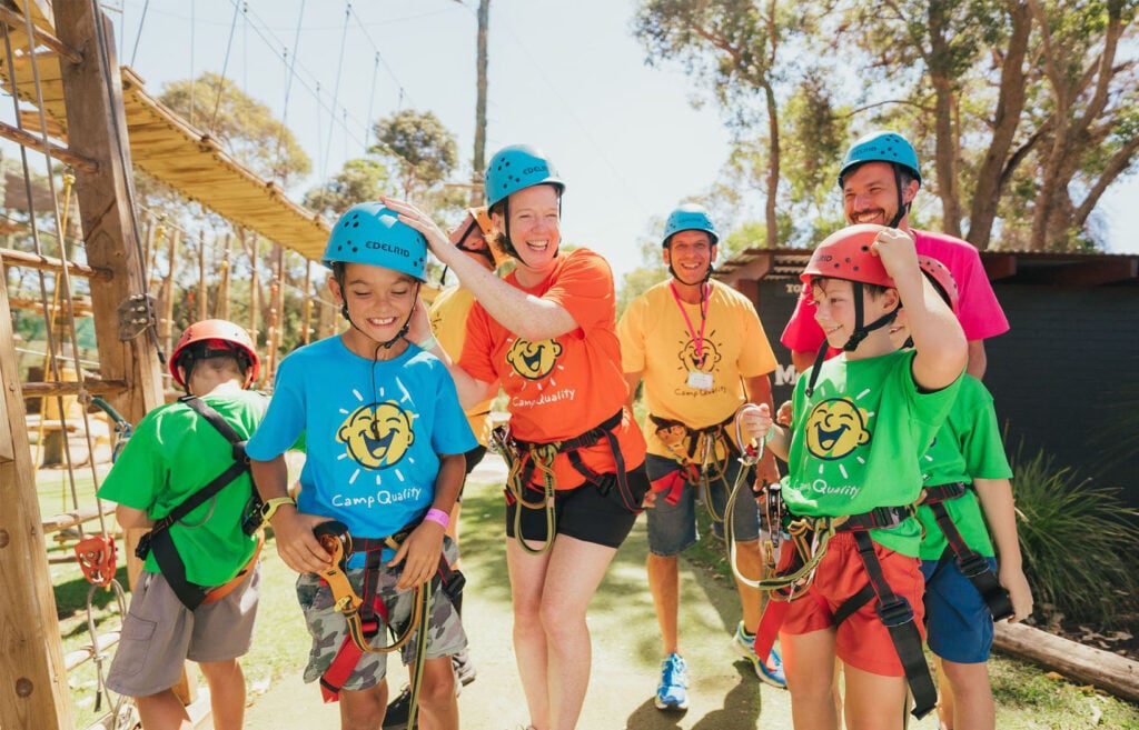 A family in hard hats and harnesses preparing to go on the flying fox at a Camp Quality family camp