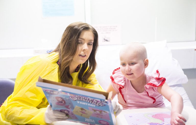 A Child Life Therapist shows a book to a child who is sat up in a hospital bed