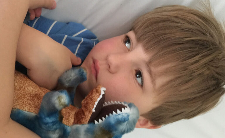 Josh in bed holding a dinosaur toy