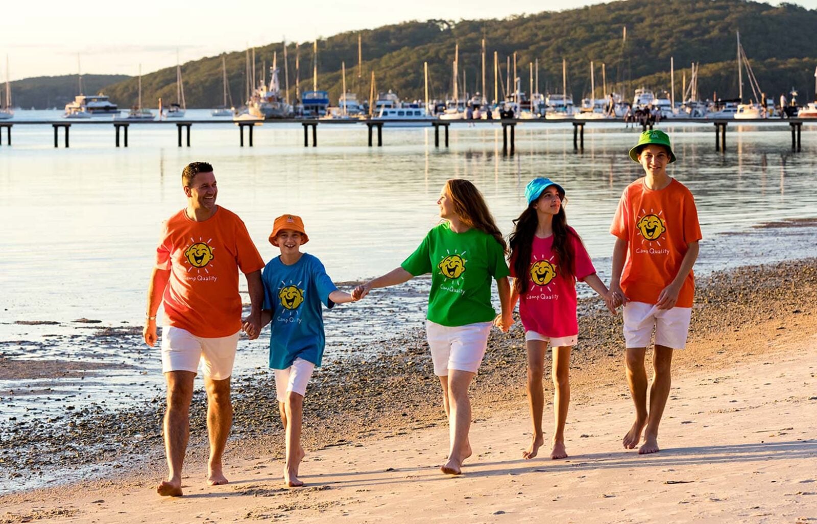 A family walks on the beach holding hands at a Camp Quality retreat