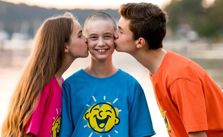 A boy smiles as his sister and brother kiss him on each cheek