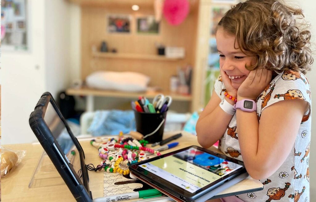A young girl looks at her tablet device with delight, hands clasped to her face