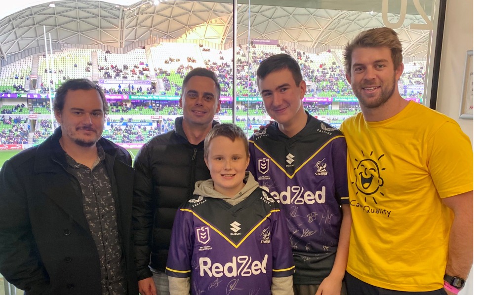 Family of 4 in Melbourne Storm jerseys at a game with player Christian Welch