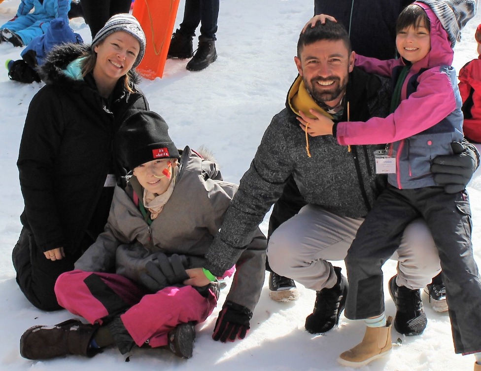 A family including a girl with a nasal gastric tube smiles and plays in the snow