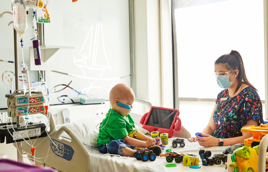 A health care professional sits at the bedside of a child with cancer in hospital