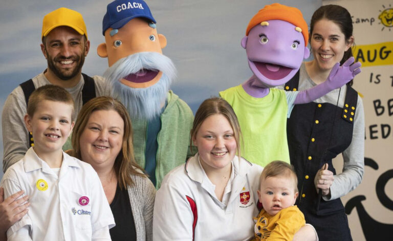 Family with kids in school uniforms smiles with the Camp Quality Puppets