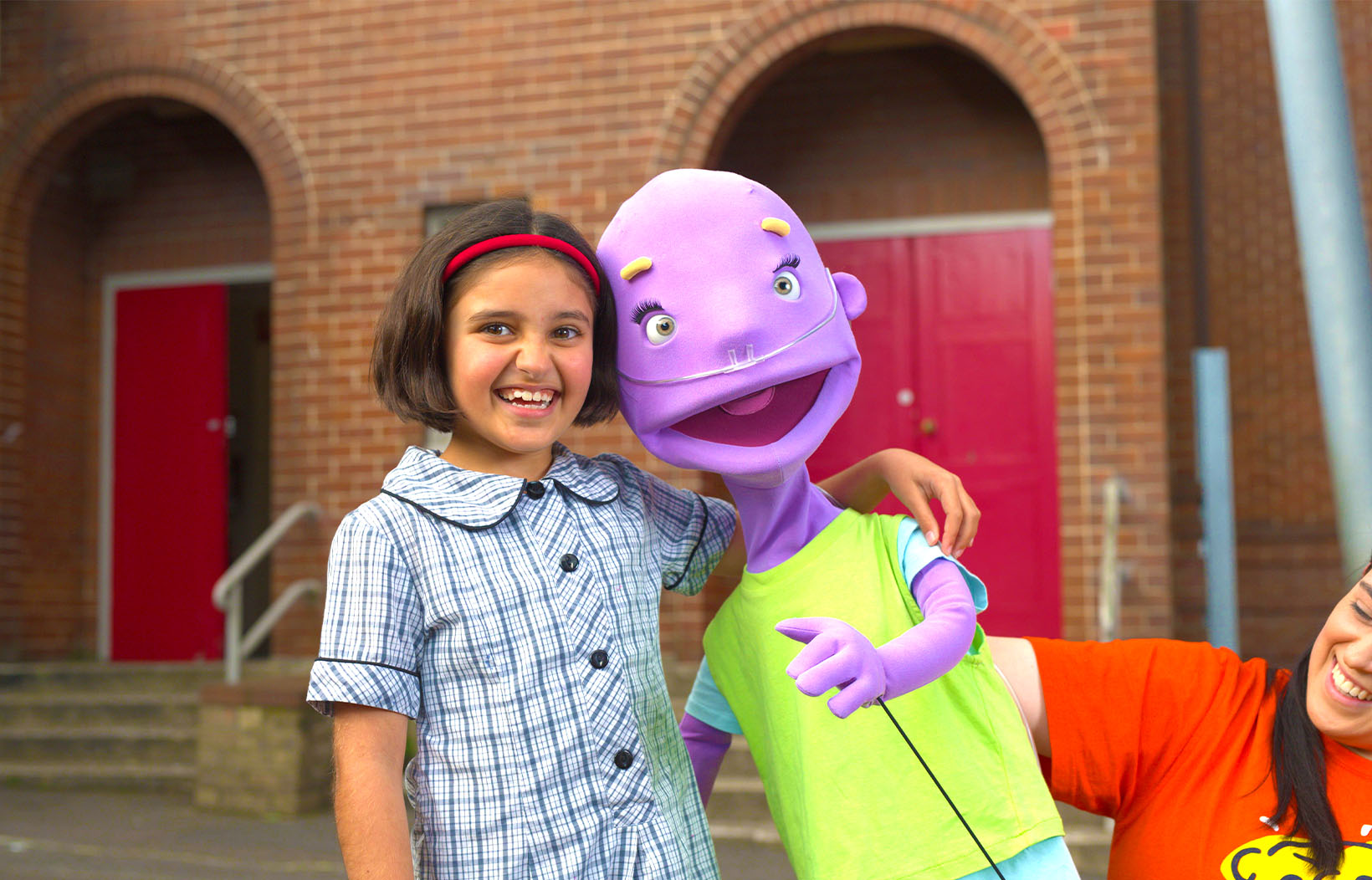Poppy smiling and hugging a purple Camp Quality puppet
