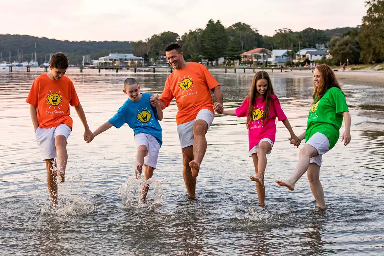 A family of 5 splash their feet in a bay at sunset