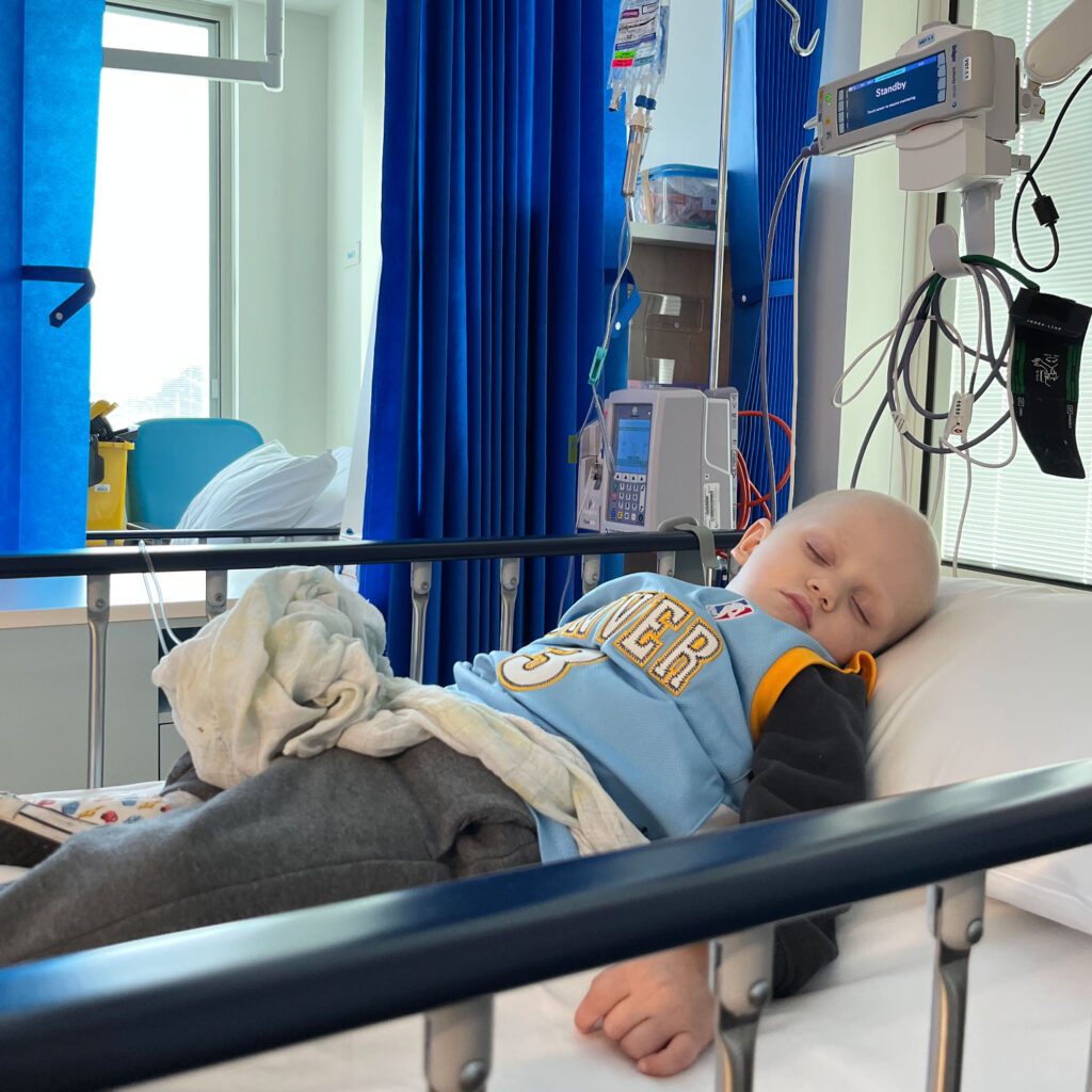 Toddler with a shaved head sleeps in hospital bed