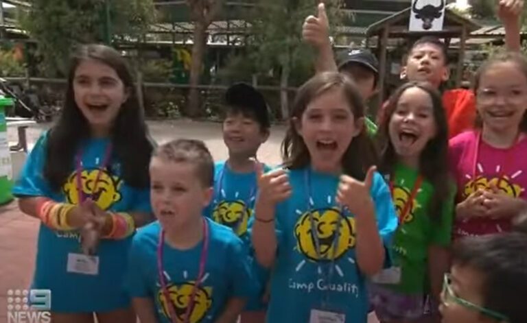 7 kids in Camp Quality shirts smile for the news camera