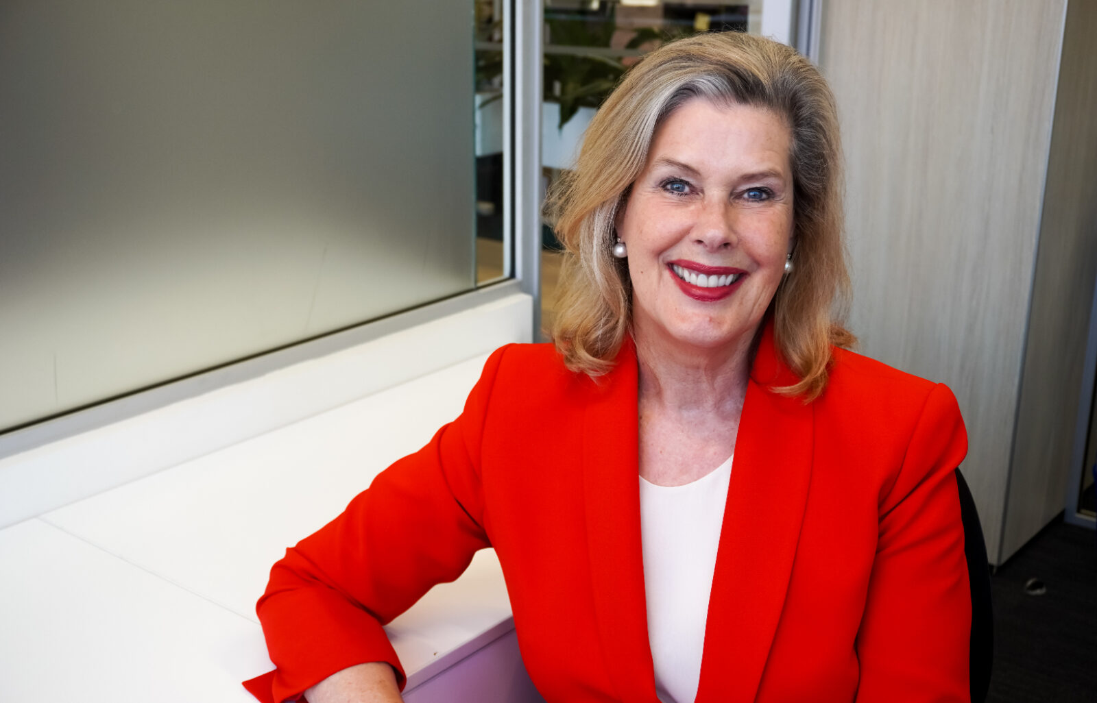 Deborah Thomas in a red suit smiles at her desk