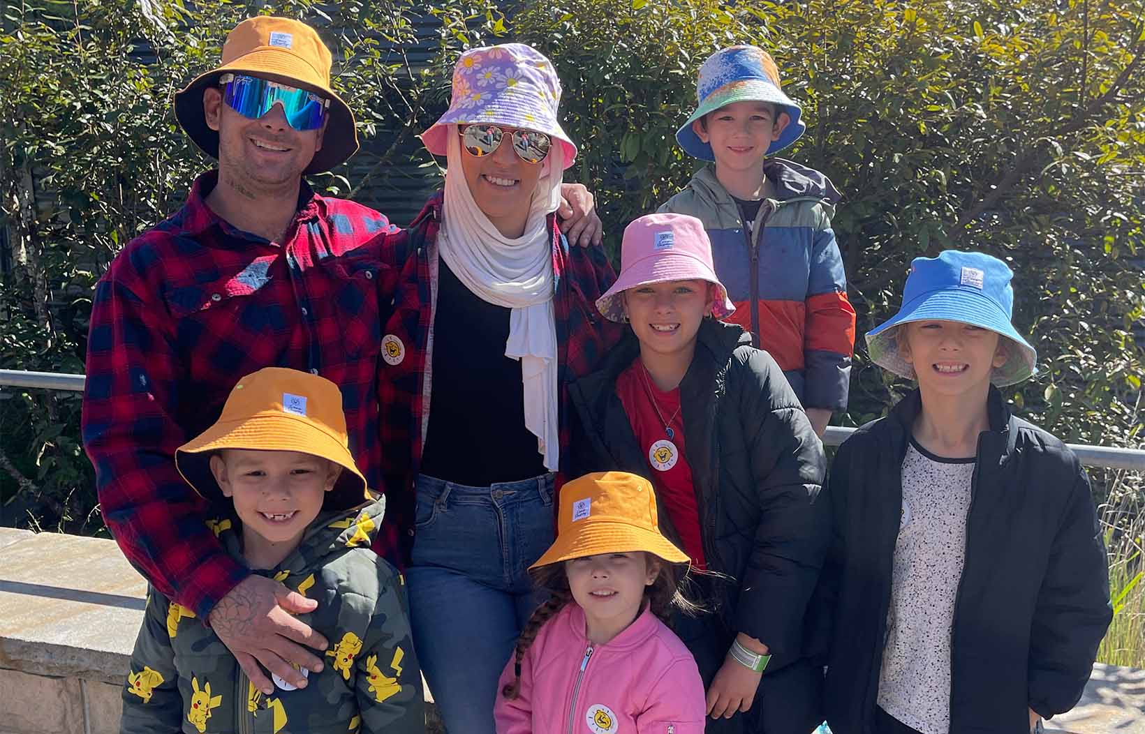 Camp Quality family all wearing bucket hats together while smiling at the camera.
